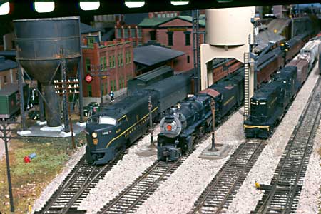 Two passenger trains are ready to depart the busy Mount Penn station, while two Geeps glide their manifest train out of town.